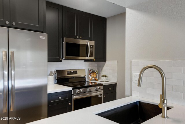 kitchen featuring stainless steel appliances, a sink, dark cabinets, and tasteful backsplash
