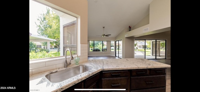 kitchen with ceiling fan, dark brown cabinetry, sink, light stone countertops, and high vaulted ceiling