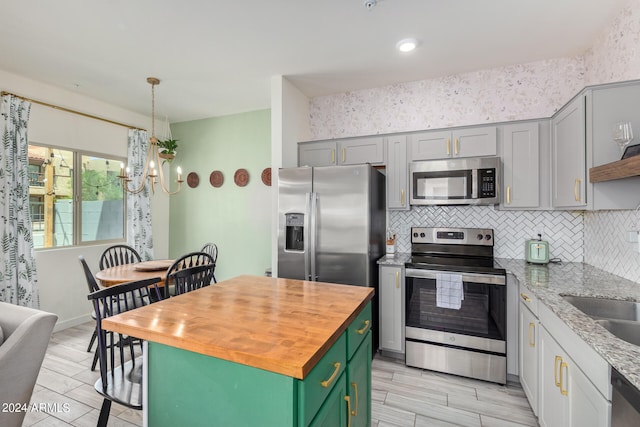 kitchen featuring a center island, hanging light fixtures, backsplash, appliances with stainless steel finishes, and a notable chandelier