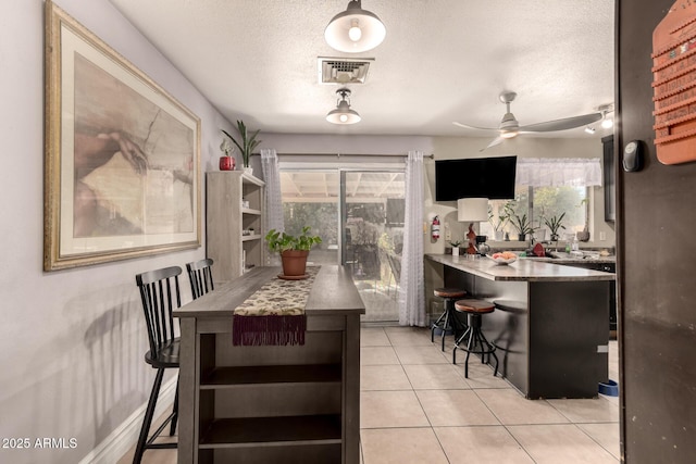 kitchen featuring a textured ceiling, ceiling fan, light tile patterned floors, and a breakfast bar area