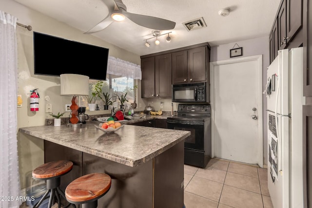 kitchen featuring black appliances, kitchen peninsula, dark brown cabinetry, a breakfast bar area, and light tile patterned floors