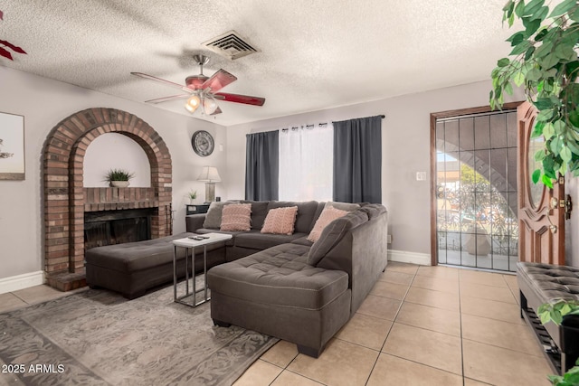 living room with a textured ceiling, ceiling fan, light tile patterned floors, and a fireplace