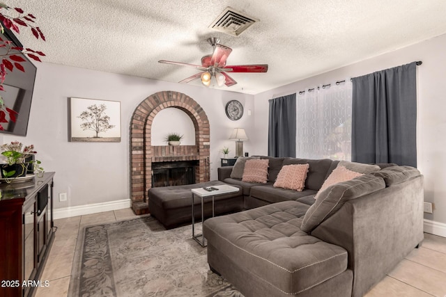 tiled living room with a brick fireplace, a textured ceiling, and ceiling fan