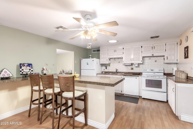4046 E Crocus Dr, Phoenix, AZ 85032 - kitchen with white appliances, dark countertops, a peninsula, light wood-style flooring, and white cabinetry