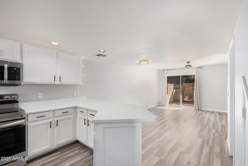 kitchen featuring ceiling fan, kitchen peninsula, light wood-type flooring, appliances with stainless steel finishes, and white cabinets