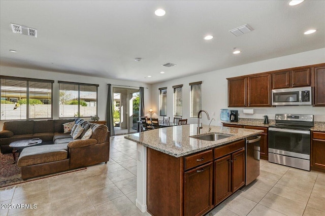 kitchen with sink, light tile patterned floors, a kitchen island with sink, stainless steel appliances, and light stone countertops