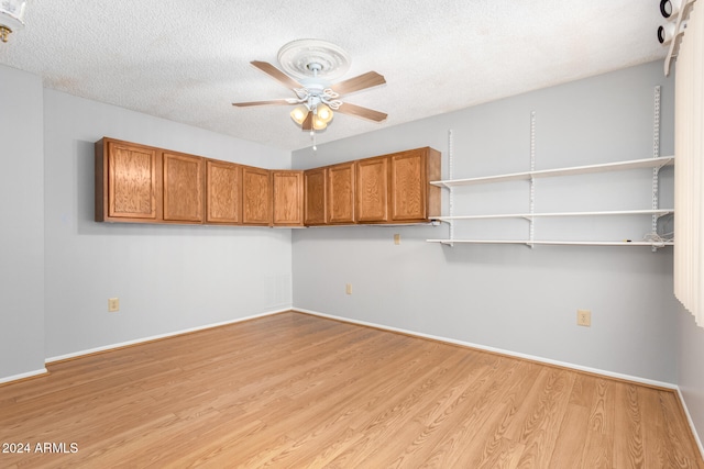 empty room with a textured ceiling, light wood-type flooring, and ceiling fan