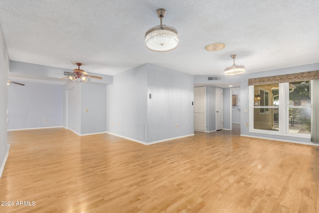 unfurnished living room featuring ceiling fan with notable chandelier, light hardwood / wood-style floors, and a textured ceiling