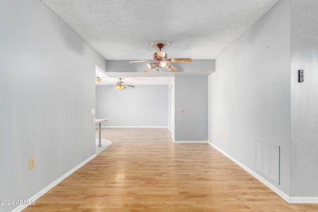 corridor with a textured ceiling and light hardwood / wood-style flooring