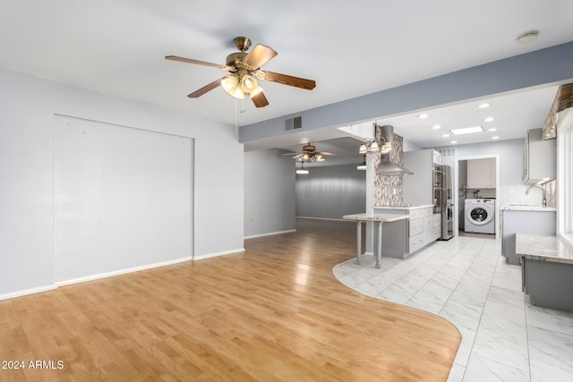 unfurnished living room featuring washer / clothes dryer, light hardwood / wood-style flooring, ceiling fan, and sink