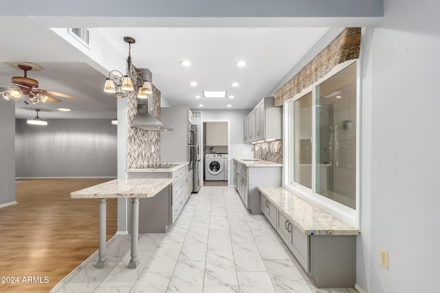 kitchen featuring pendant lighting, a kitchen breakfast bar, gray cabinets, tasteful backsplash, and washer / clothes dryer