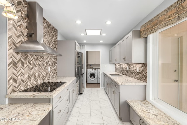 kitchen with gray cabinetry, wall chimney range hood, sink, black electric cooktop, and washing machine and clothes dryer