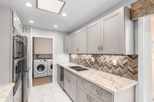 kitchen with light stone counters, stainless steel appliances, washer and clothes dryer, sink, and gray cabinets