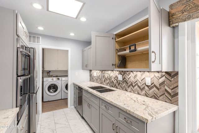 kitchen with washing machine and clothes dryer, gray cabinets, light stone counters, and sink