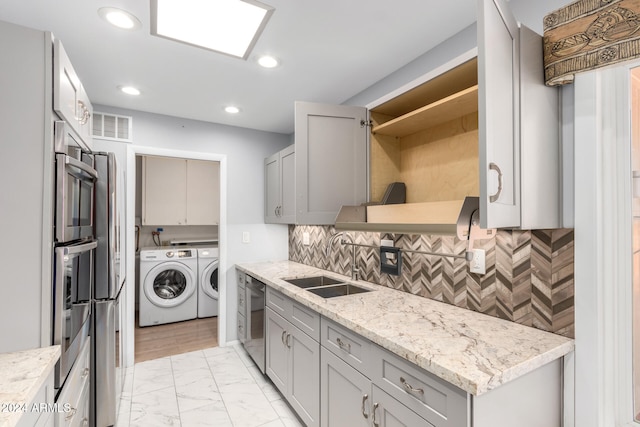 kitchen with washer and dryer, appliances with stainless steel finishes, light stone counters, and sink