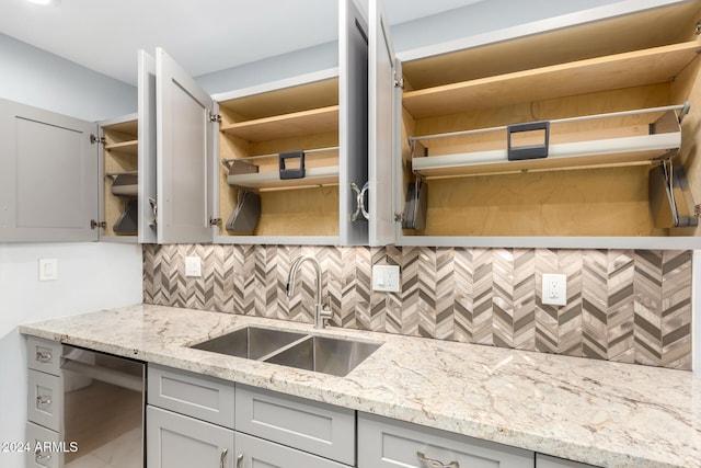 kitchen featuring stainless steel dishwasher, gray cabinetry, light stone countertops, and sink