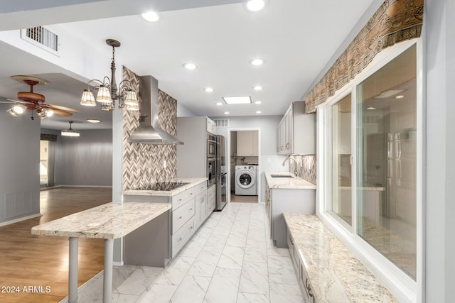 kitchen with pendant lighting, wall chimney exhaust hood, washer / clothes dryer, and tasteful backsplash