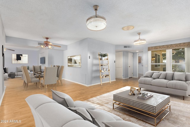 living room with ceiling fan with notable chandelier, a textured ceiling, and light wood-type flooring