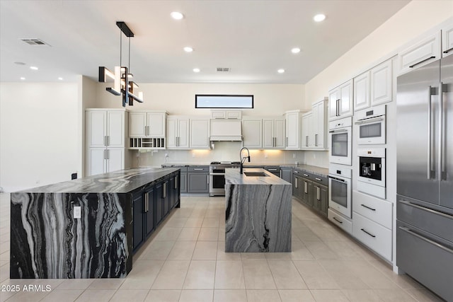 29215 N 136th St, Scottsdale, AZ 85262 - kitchen featuring high end appliances, a large island with sink, light tile patterned floors, decorative light fixtures, and dark stone counters