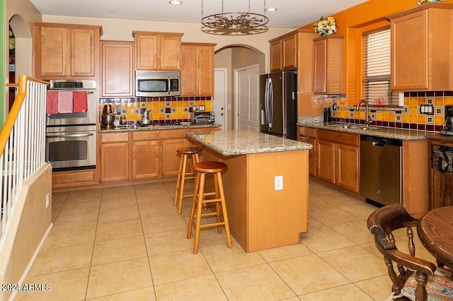 kitchen with light tile patterned floors, backsplash, a kitchen island, sink, and stainless steel appliances