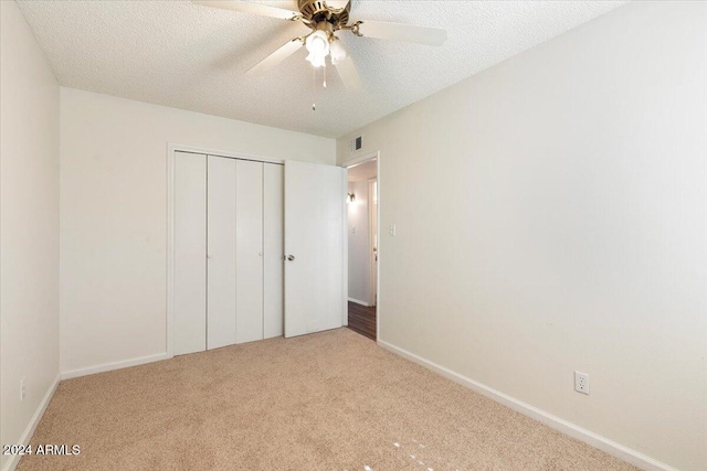 unfurnished bedroom featuring ceiling fan, a textured ceiling, a closet, and light colored carpet