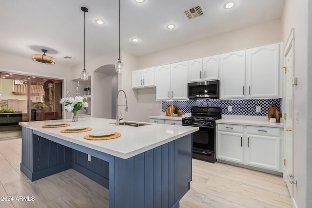 kitchen with black gas range, an island with sink, pendant lighting, and light hardwood / wood-style floors