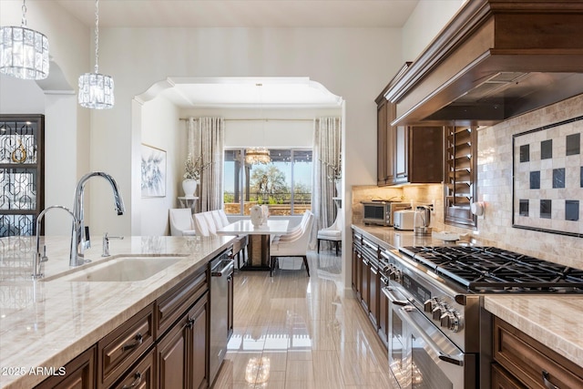 kitchen featuring backsplash, premium range hood, stainless steel appliances, sink, and a notable chandelier