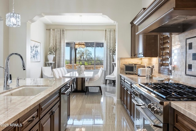 kitchen featuring an inviting chandelier, sink, appliances with stainless steel finishes, light stone counters, and custom range hood