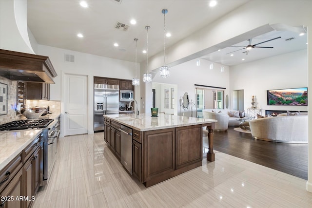 kitchen featuring light stone counters, a spacious island, sink, pendant lighting, and built in appliances