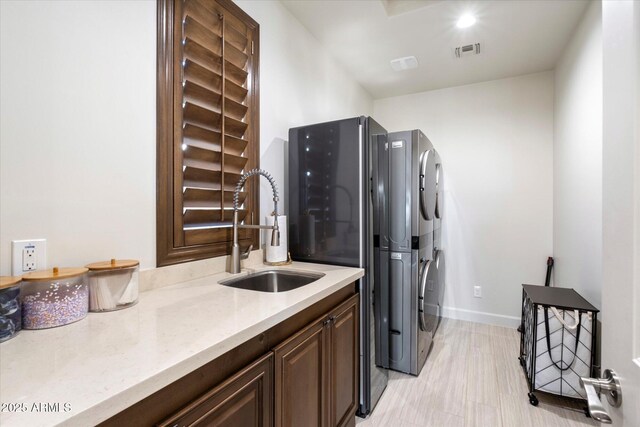 laundry room featuring cabinets, stacked washing maching and dryer, and sink