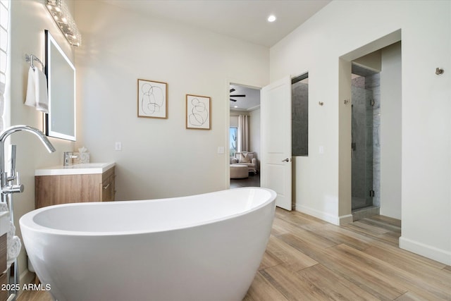 bathroom with plus walk in shower, vanity, hardwood / wood-style flooring, and ceiling fan