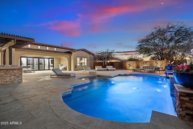 pool at dusk featuring a patio area, pool water feature, and an outdoor hangout area