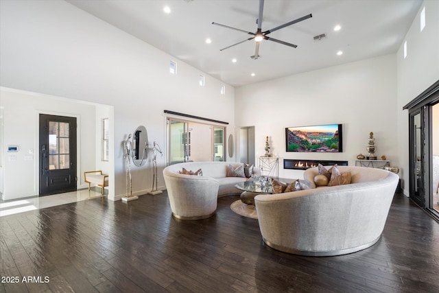 living room with a high ceiling, dark hardwood / wood-style flooring, and ceiling fan