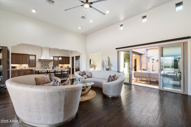 living room featuring ceiling fan, a towering ceiling, and dark wood-type flooring