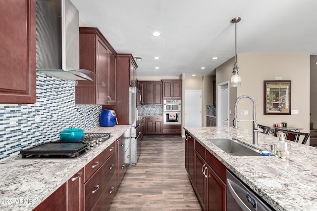 kitchen featuring sink, decorative light fixtures, light stone counters, and wall chimney range hood