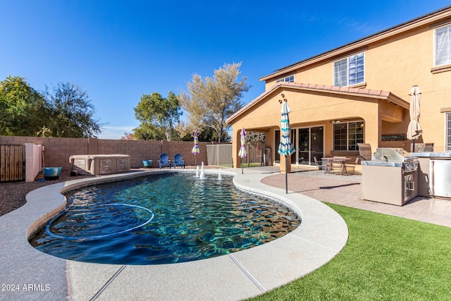 view of swimming pool with pool water feature, an outdoor kitchen, and a patio area