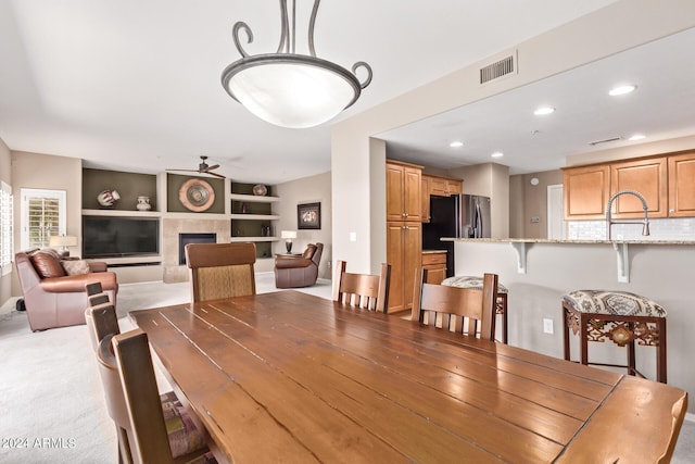 dining area featuring ceiling fan, built in shelves, sink, light colored carpet, and a fireplace