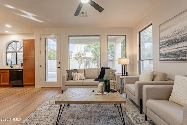 living room featuring ceiling fan, sink, and light wood-type flooring