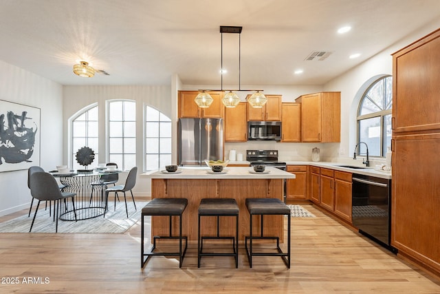 kitchen with sink, hanging light fixtures, a center island, stainless steel appliances, and light hardwood / wood-style flooring