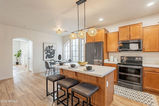 kitchen featuring a kitchen island, appliances with stainless steel finishes, pendant lighting, a kitchen bar, and light hardwood / wood-style flooring