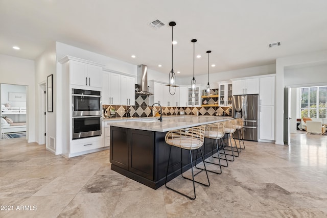 kitchen featuring stainless steel appliances, wall chimney range hood, hanging light fixtures, white cabinetry, and a large island