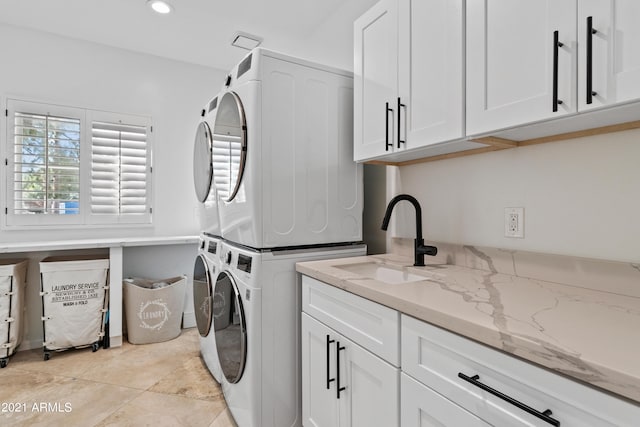 laundry area featuring cabinets, light tile patterned floors, sink, and stacked washer and dryer