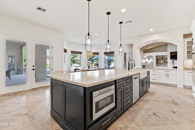 kitchen with stainless steel appliances, sink, pendant lighting, white cabinetry, and a center island with sink