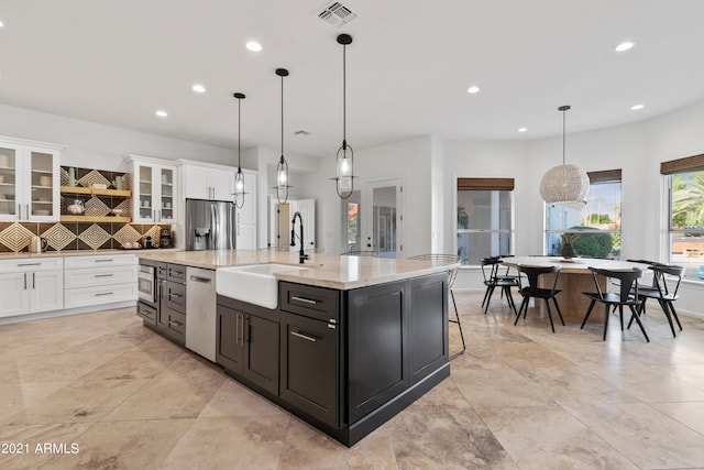 kitchen with appliances with stainless steel finishes, pendant lighting, sink, and an island with sink