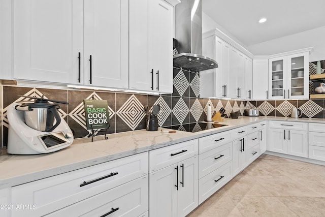 kitchen with light stone countertops, wall chimney range hood, white cabinetry, and decorative backsplash