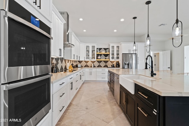 kitchen with decorative backsplash, a kitchen island with sink, stainless steel appliances, hanging light fixtures, and white cabinetry