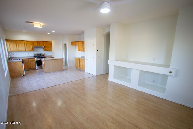 kitchen with light hardwood / wood-style floors, a center island, sink, and stainless steel gas range oven