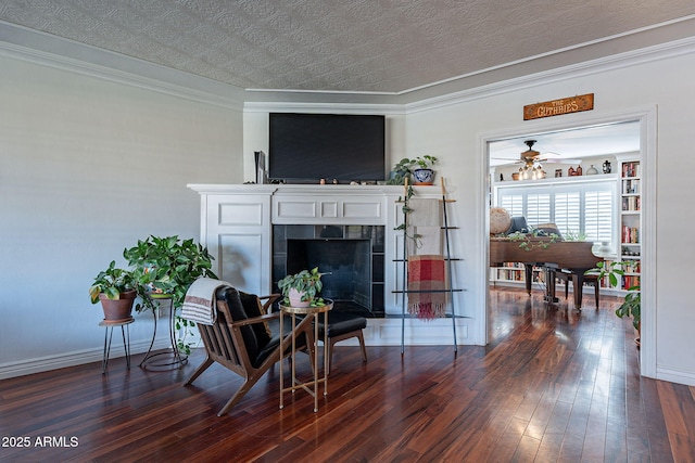 living area featuring dark wood-type flooring, ornamental molding, a tile fireplace, and a textured ceiling