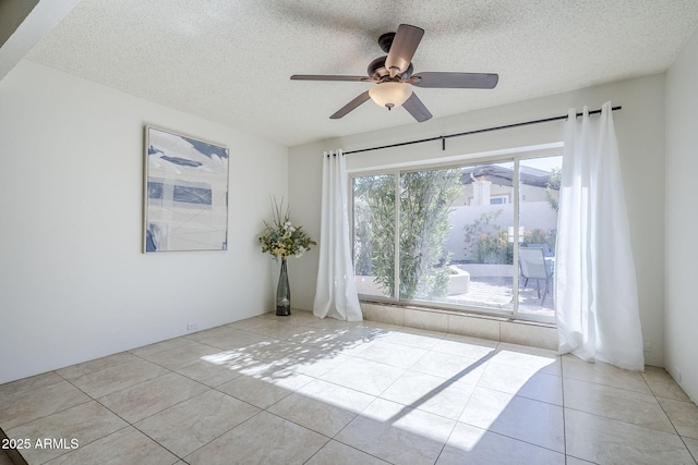 empty room with ceiling fan, light tile patterned floors, and a textured ceiling