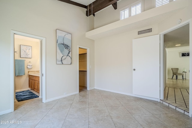 empty room featuring beamed ceiling, light tile patterned flooring, and a towering ceiling